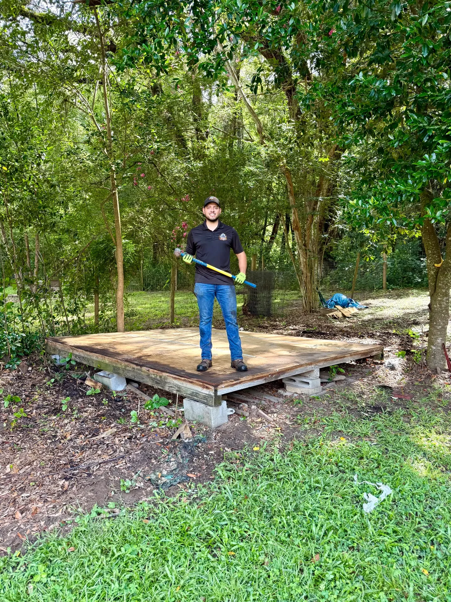 Tally Junk Removal owner standing with a sledgehammer on the bare concrete slab left after a backyard shed was torn down