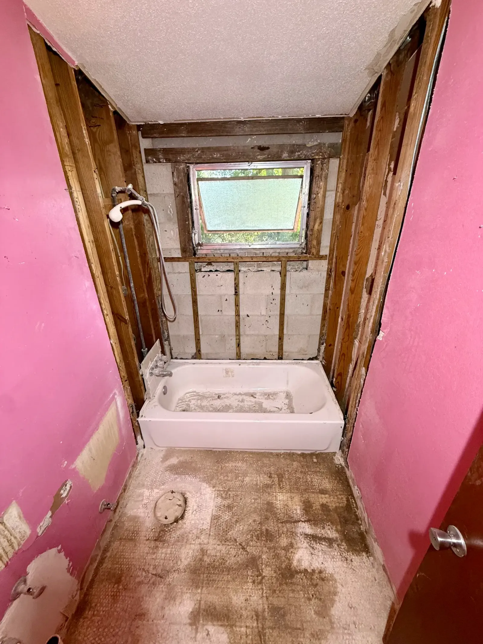 Same bathroom with wall studs exposed and floor finish stripped; bathtub remains