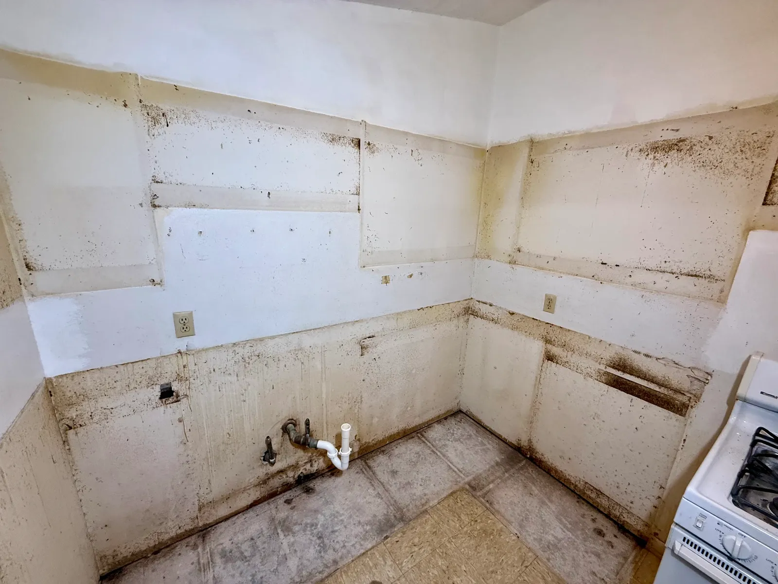 Kitchen walls and plumbing exposed after cabinet and counter removal; white range remains