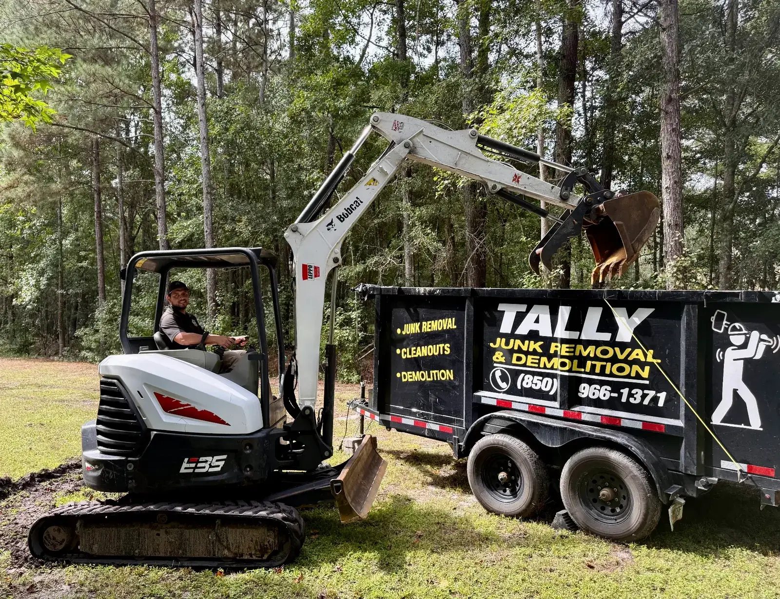 Mauricio Chavez operating a Bobcat E35 mini excavator beside the Tally Junk Removal and Demolition branded trailer