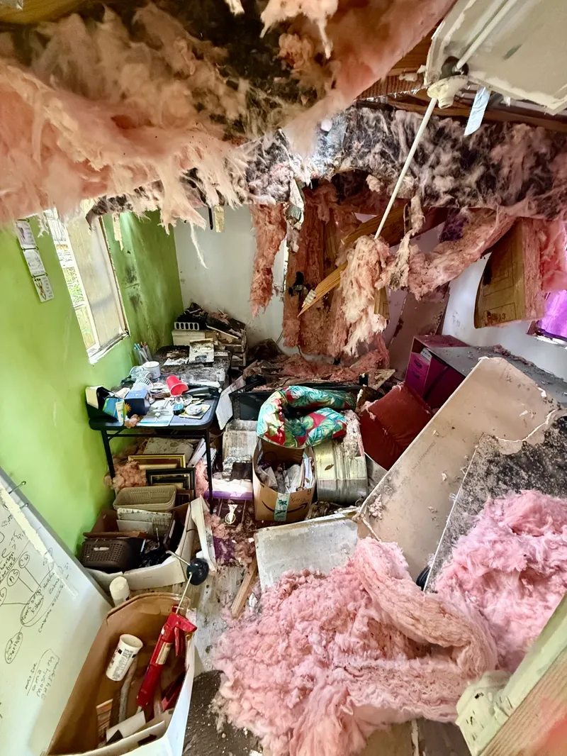 Room with collapsed ceiling insulation, damaged drywall, and soaked contents spread across the floor awaiting debris removal