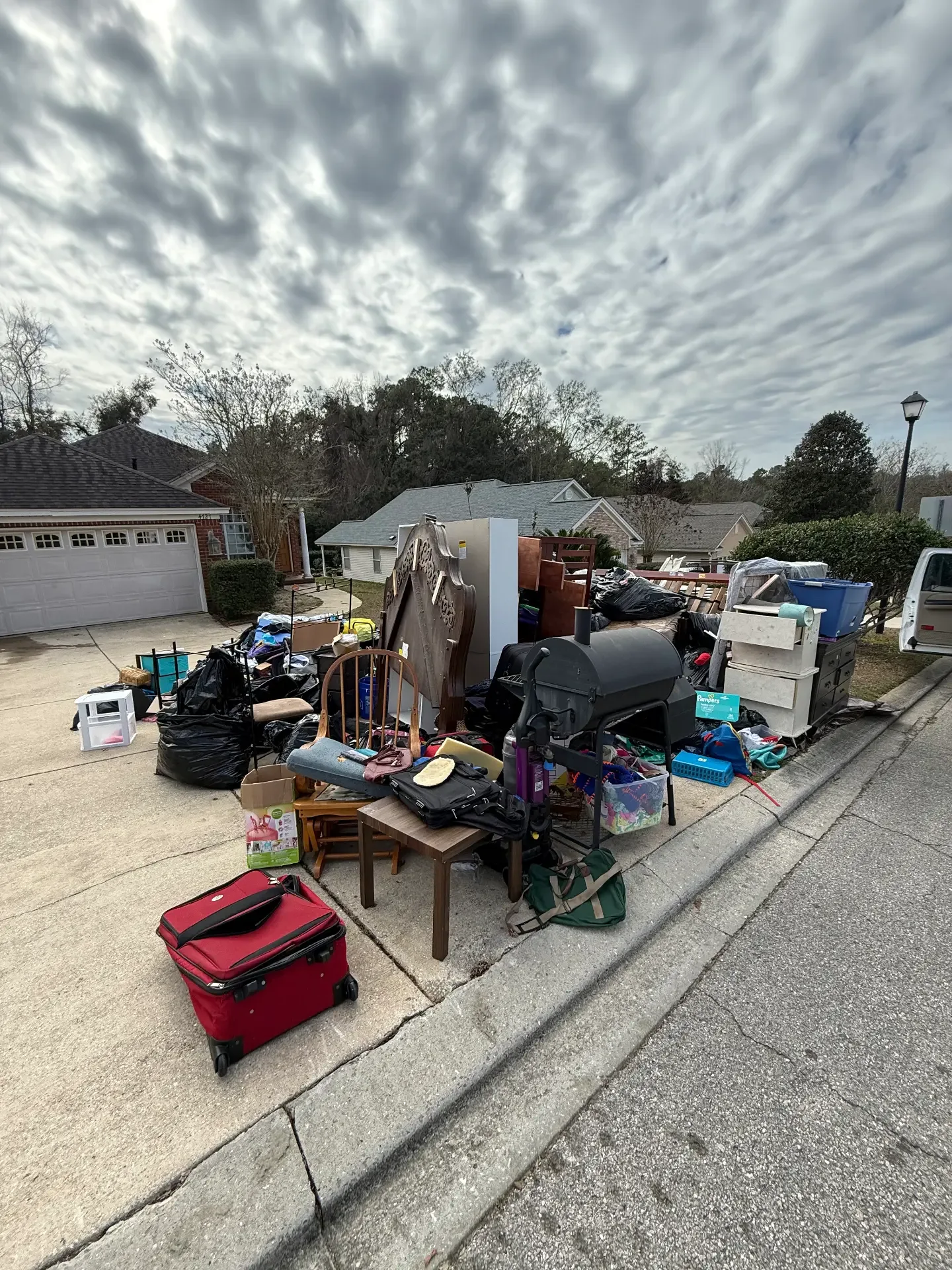 Driveway and curbside pile of furniture, boxes, a grill, and bagged household items staged for haul away outside a Tallahassee home