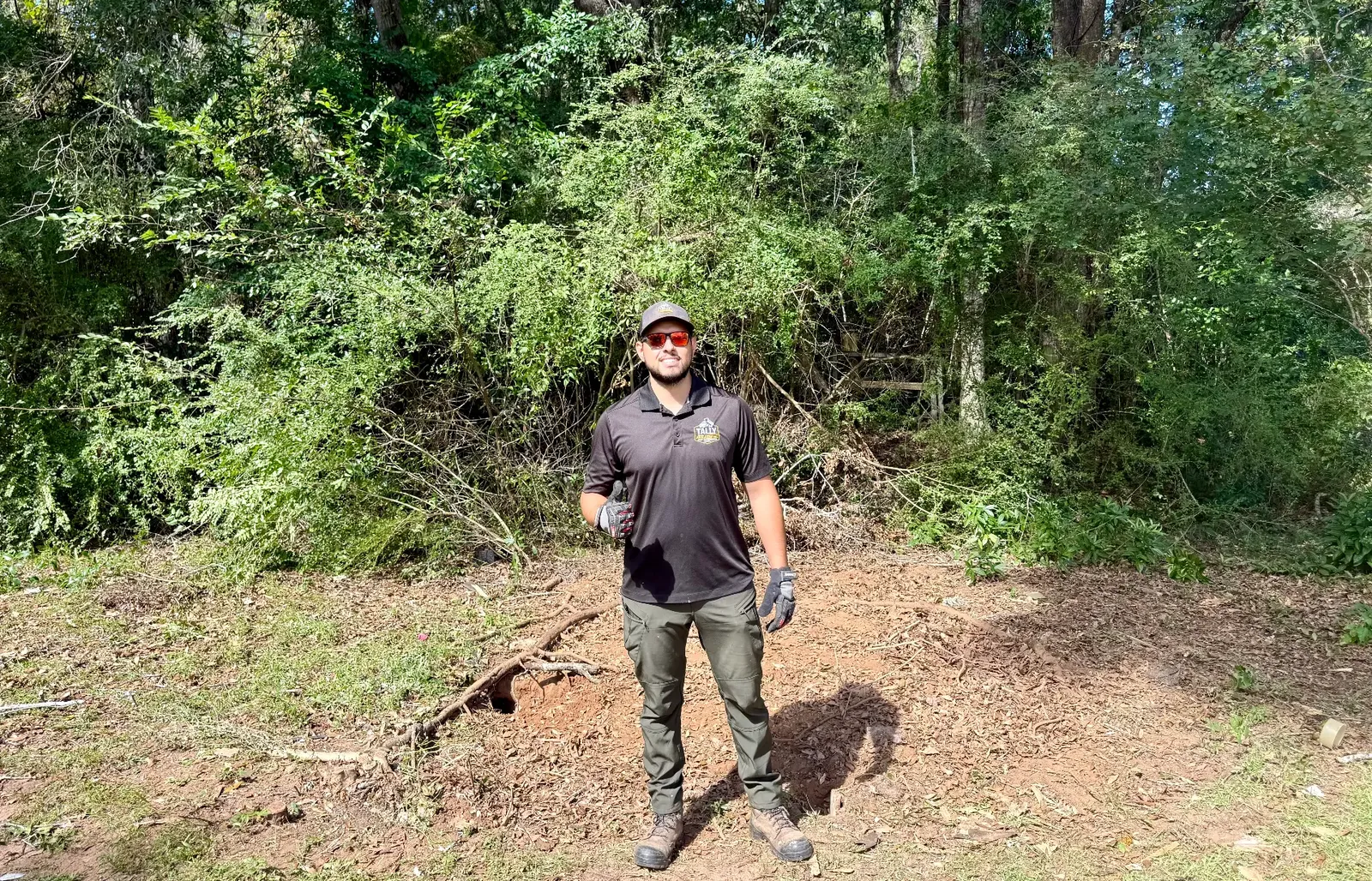 Owner standing in the former shed footprint after structure removal with leaves and brush visible
