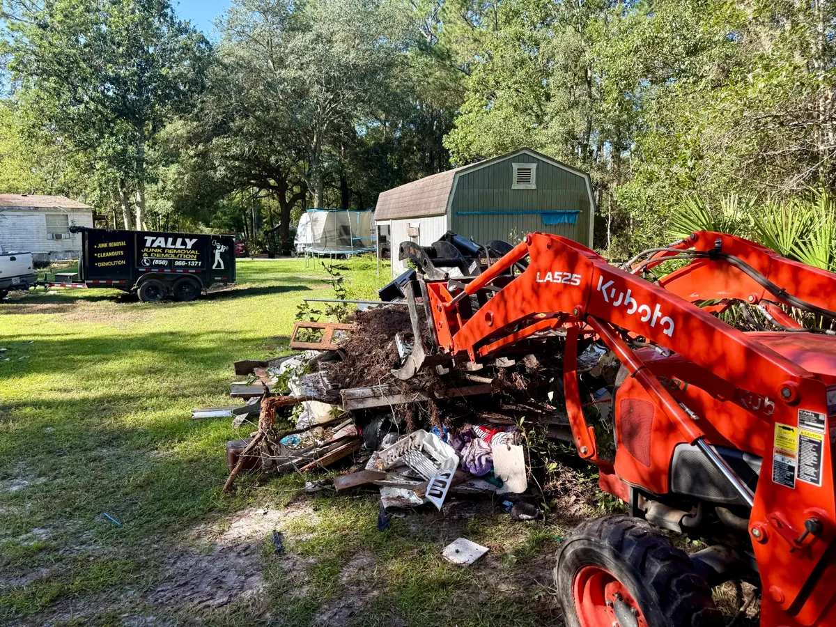 Tractor loading mixed yard debris and junk into the Tally Junk Removal dump trailer