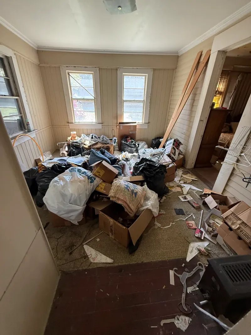 Bedroom packed with cardboard boxes, filled trash bags, and loose household items covering the floor