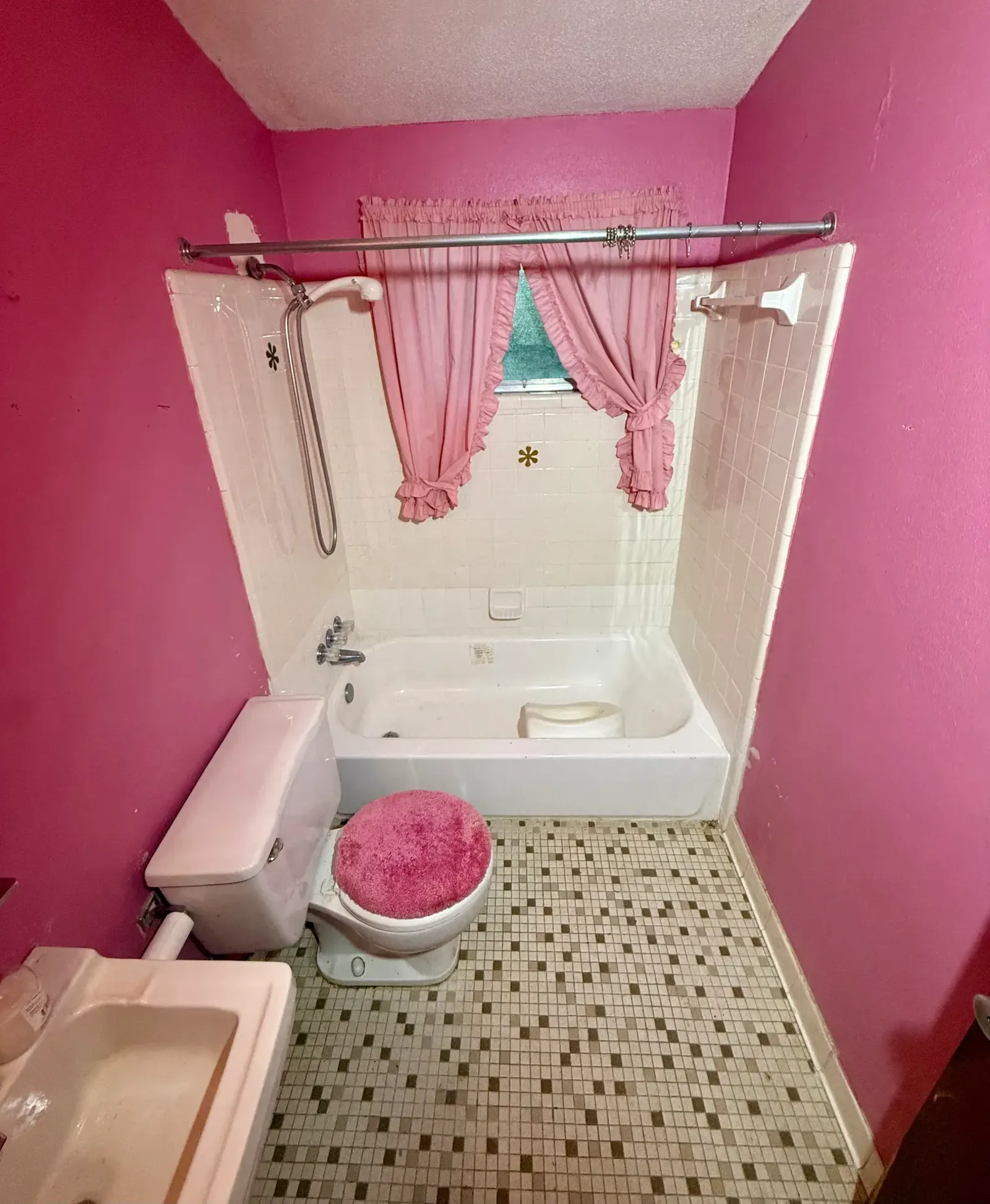 Pink bathroom with tiled bathtub surround and patterned floor before selective tear-out