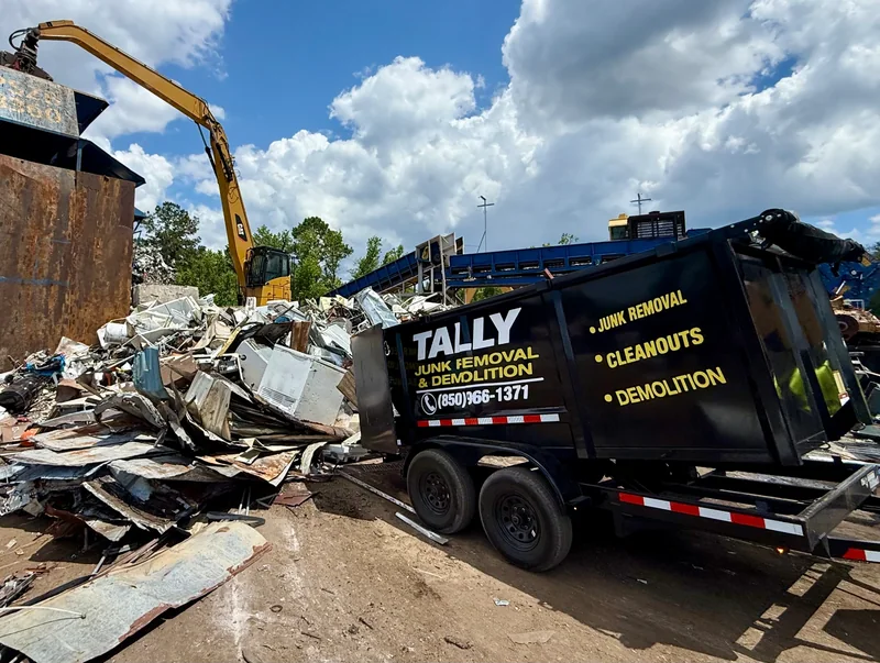 Tally Junk Removal branded dump trailer unloading construction scrap at a metal recycling yard