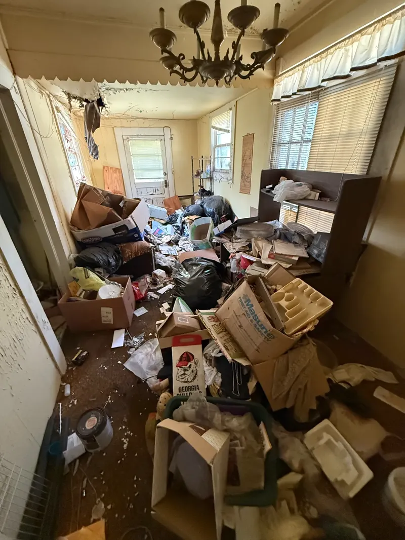 Dining room stacked shoulder high with boxes, bags, and paper clutter under a hanging chandelier