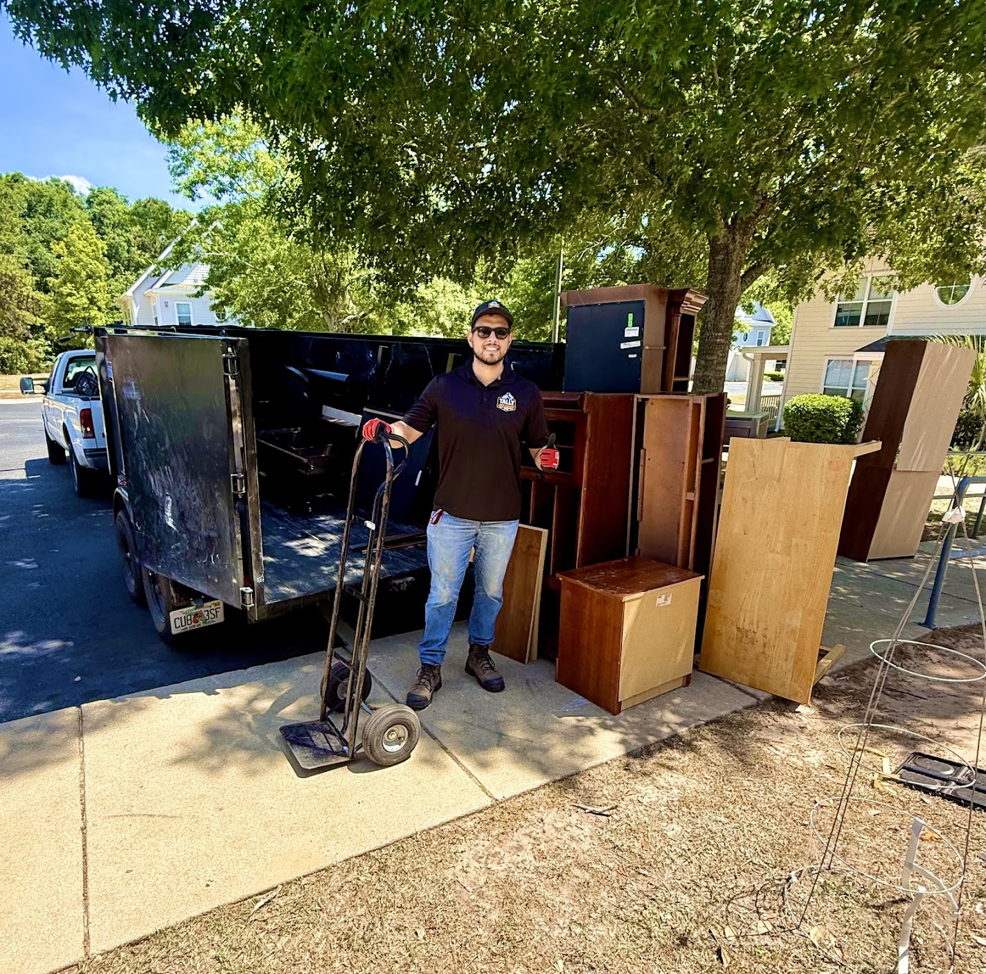 Tally Junk Removal team member loading old furniture and cabinets into the dump trailer at a residential driveway