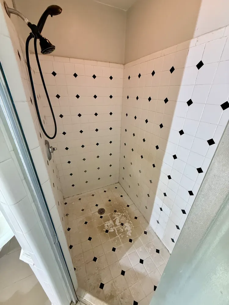 White tile shower with black diamond accents before demolition