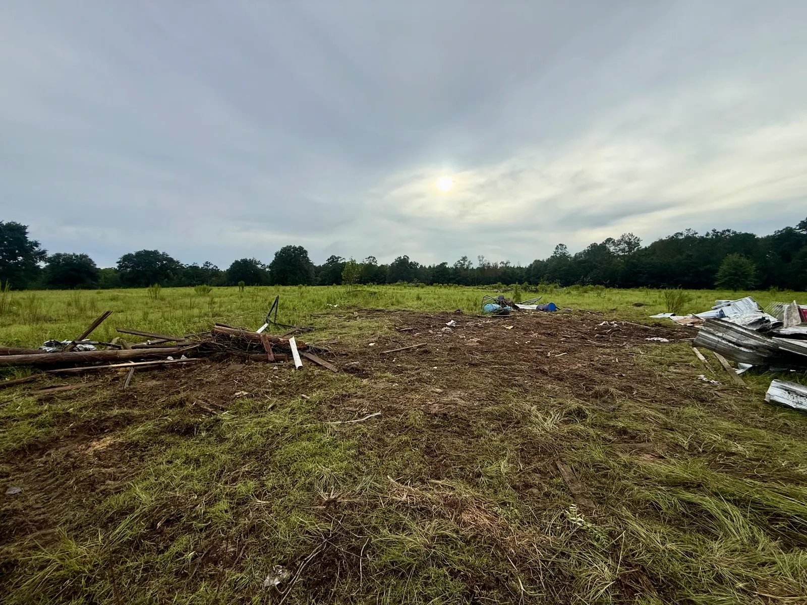 Open field with a large patch of ground cleared of debris, a few remaining piles of lumber and metal at the edges
