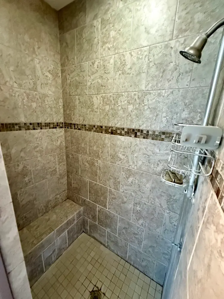 Beige tile shower with mosaic band and bench before demolition