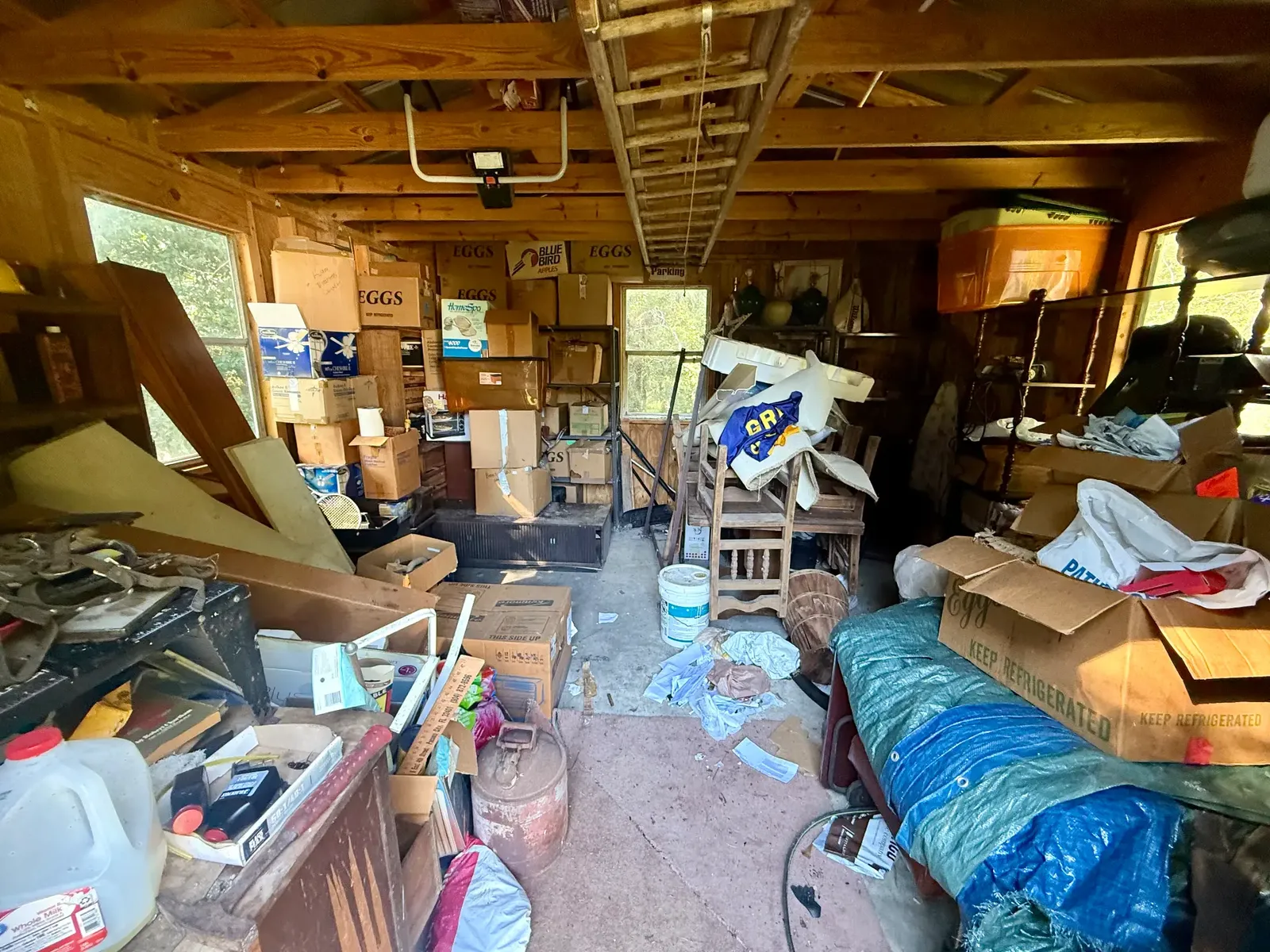Wooden shed room filled with boxes, furniture, and loose stored contents