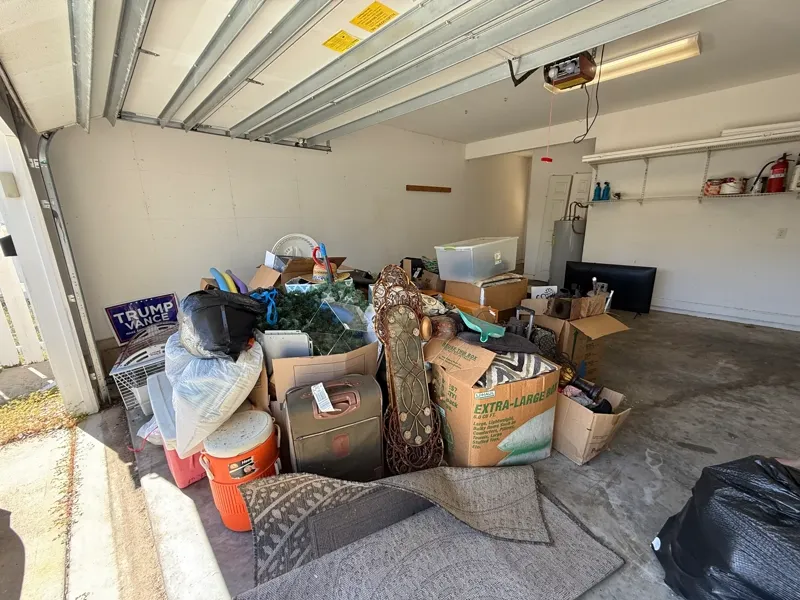 Garage cleanout in progress with boxes, luggage, a rolled rug, and stored household items gathered on one side